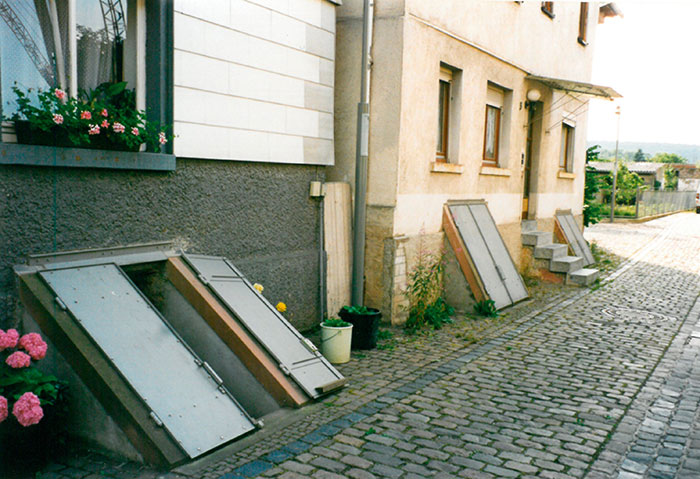 Dieses Bild zeigt zwei aneinandergrenzende Häuser, deren Kellerabgang durch Klappen (Flügeltüren) abgedichtet und verschlossen werden können.