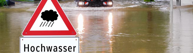 Warnschild Hochwasser vor überfluteter Straße